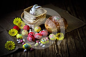 Traditional holiday composition. Hand painting Easter eggs with orthodox sweet bread on a dark wooden table. With rabbit figure.