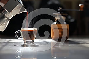 Traditional home brew espresso coffee pouring into a small cup with grinder on the dark background by the morning light with copy