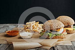 traditional homemade cheeseburgers on baking paper with french fries, ketchup