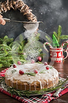 Traditional homemade Christmas cake with garnish cranberry and rosemary on decorative plate. Powdering with icing sugar.