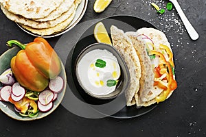 Traditional homemade flat breads for a snack with fresh seasonal vegetables, herbs and yoghurt sauce with olive oil and