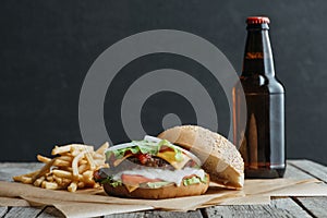 traditional homemade hamburger, french fries and bottle of beer on baking paper
