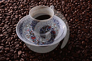 Traditional hot coffee cup with beans over a black background.