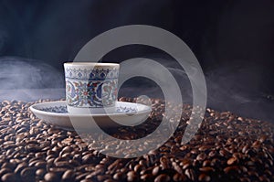 traditional hot coffee cup with beans and smoke steam over a black background.