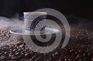 traditional hot coffee cup with beans and smoke steam over a black background.