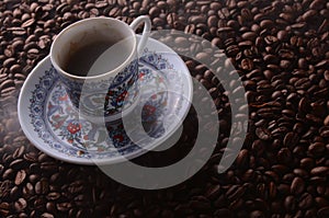 traditional hot coffee cup with beans and smoke steam over a black background.