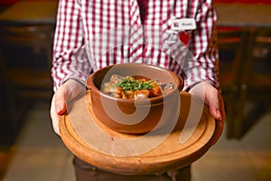 Traditional hot goulash soup. Waiter serving vegetable stew in a pot. Concept for a tasty meal. Restaurant service.