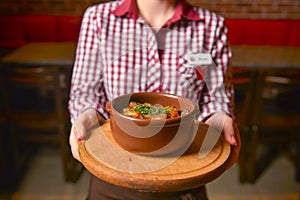 Traditional hot goulash soup. Waiter serving vegetable stew in a pot. Concept for a tasty meal. Restaurant service.