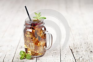 Traditional iced tea with lemon, mint leaves and ice cubes in glass jar on rustic wooden table background