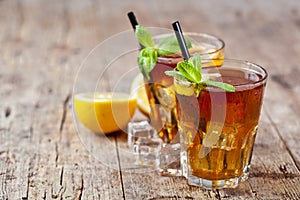 Traditional iced tea with lemon, mint leaves and ice cubes in two glasses on rustic wooden table background