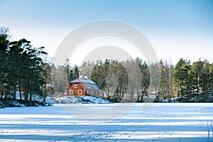 Traditional idyllic Swedish red wooden timber cabin house paint with falu red paint in winter landscape with frozen lake