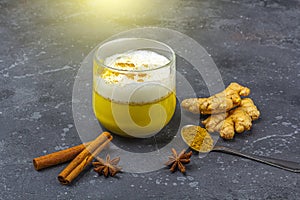Traditional Indian drink turmeric milk is golden milk in glass mug with  turmeric and root ginger, cinnamon, anis star on dark