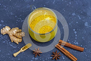 Traditional Indian drink turmeric milk is golden milk in glass mug with  turmeric and root ginger, cinnamon, anis star on dark