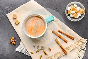 Traditional Indian masala tea chai with milk and spices on napkin on dark stone background with ingredients above