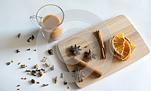 Traditional Indian masala tea with spices. Anise, star anise, cinnamon, pepper, milk. White background. Wooden plank. Top view
