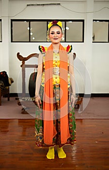 a traditional Indonesian dancer standing in a yellow costume and an orange scarf hanging down her body