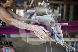 Traditional Isan Thai silk weaving. Hand of an old woman weaving silk in traditional way at manual loom. Kalasin, Thailand