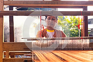 Traditional Isan Thai silk weaving. old woman hand weaving silk Akkanee in traditional way at manual loom. Phu fabric dyeing