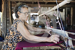 Traditional Isan Thai silk weaving. old woman hand weaving silk in traditional way at manual loom. Kalasin, Thailand