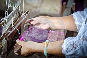 Traditional Isan Thai silk weaving. old woman hand weaving silk in traditional way at manual loom. Thailand . Selective focus