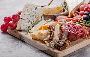 Traditional italian antipasto plate. Assorted cheeses on wooden cutting board. Brie cheese, cheddar slices, gogonzola, walnuts