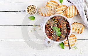Traditional Italian Caponata and toast on a wooden white table.