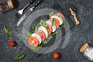 Traditional Italian Caprese Salad - sliced tomatoes, mozzarella cheese and basil on stone background, top view