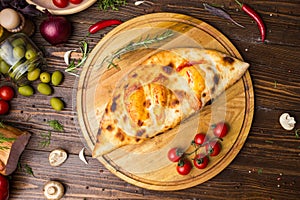 Traditional italian closed pizza Calzone with basil leaves on wooden background photo