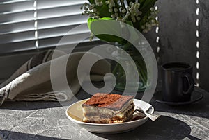 Traditional Italian dessert tiramisu, coffee and a bouquet of lilies of the valley on a gray concrete background.