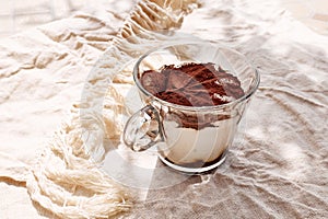 Traditional Italian dessert Tiramisu in a glass cup on a table with linen tablecloth. National cuisine recipe.