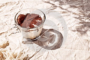 Traditional Italian dessert Tiramisu in a glass cup on a table with linen tablecloth. National cuisine recipe.