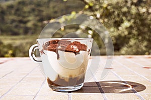 Traditional Italian dessert Tiramisu in a glass cup on a tile table in the garden. National cuisine recipe.