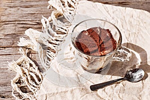 Traditional Italian dessert Tiramisu in a glass cup on a wooden table with linen tablecloth. National cuisine recipe.