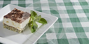 Traditional Italian dessert tiramisu served on a white plate with a mint leaf in a restaurant. Italian cuisine, dessert.