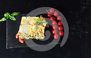 Traditional Italian dish of lasagna with meat, spinach, cheese close-up on a slate plate on a black background. horizontal