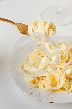 Traditional Italian pasta - Fetuccini Alfredo on a white table with golden appliances