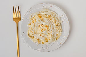 Traditional Italian pasta - Fetuccini Alfredo on a white table with golden appliances