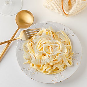 Traditional Italian pasta - Fetuccini Alfredo on a white table with golden appliances