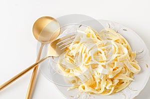 Traditional Italian pasta - Fetuccini Alfredo on a white table with golden appliances