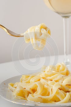 Traditional Italian pasta - Fetuccini Alfredo on a white table with golden appliances