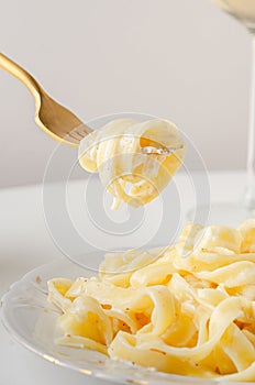 Traditional Italian pasta - Fetuccini Alfredo on a white table with golden appliances