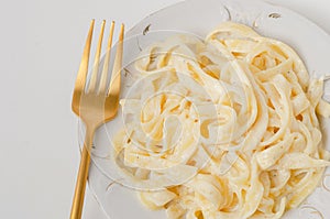 Traditional Italian pasta - Fetuccini Alfredo on a white table with golden appliances