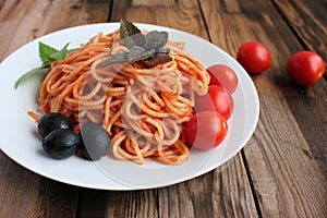 Traditional Italian pasta and ingredients on the white plate on rustic wooden table background. Long spaghetti with tomato sauce,