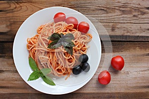 Traditional Italian pasta and ingredients on the white plate on rustic wooden table background. Long spaghetti with tomato sauce,