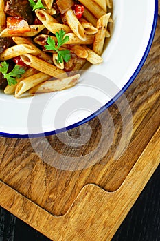 Traditional Italian pasta with meat and vegetables and parsley on white plate with dark wooden background