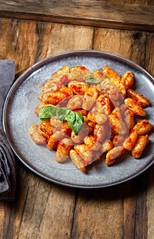 Traditional Italian potato Gnocchi with tomato sauce and fresh basil on blue plate on wooden background