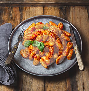 Traditional Italian potato Gnocchi with tomato sauce and fresh basil on blue plate on wooden background