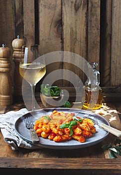 Traditional Italian potato Gnocchi with tomato sauce and fresh basil with glas of white wine. rustic background