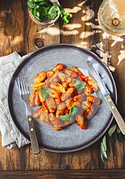 Traditional Italian potato Gnocchi with tomato sauce and fresh basil with glas of white wine. rustic background