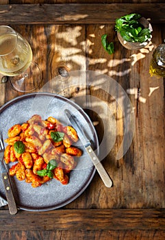 Traditional Italian potato Gnocchi with tomato sauce and fresh basil with glas of white wine. rustic background